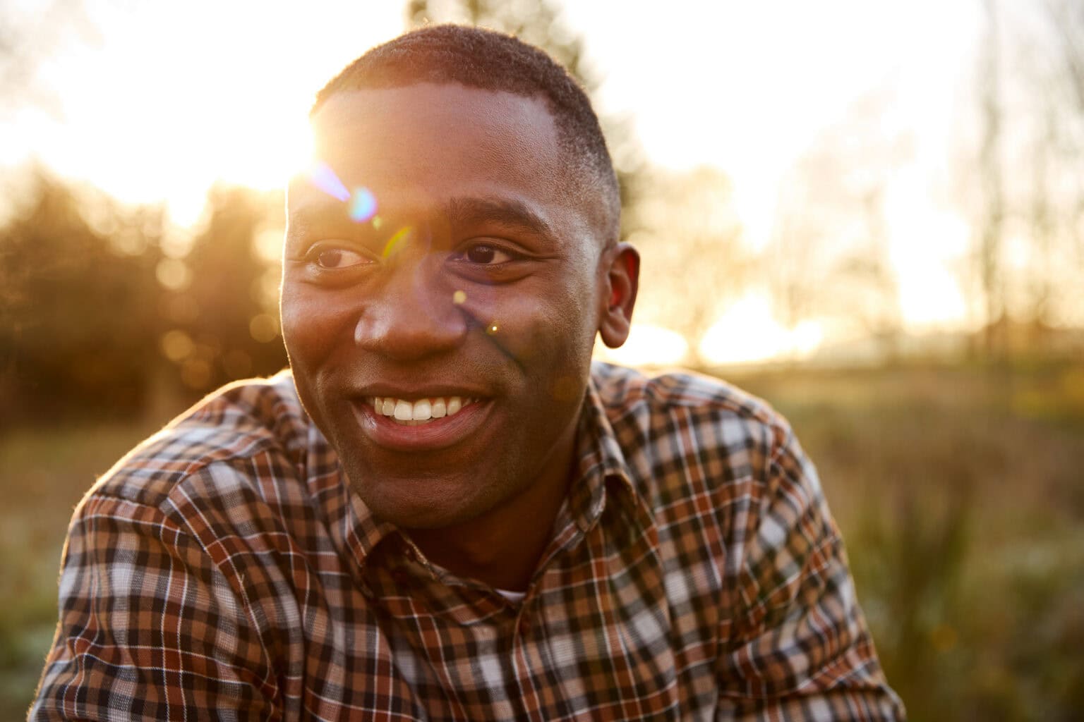 Man in a plaid shirt smiling outdoors in evening sunlight